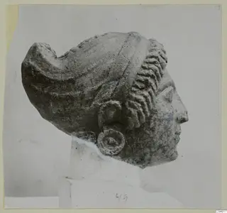 Limestone head from Arsos in profile, facing right, with a layered hair roll and a disc earring.