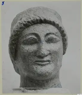 Limestone head of a figure with a band of curled hair across the forehead, photographed against a pale background.