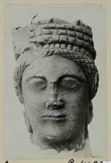 Stone statue head from Arsos, shown from the front, with a tall patterned headdress and a damaged nose