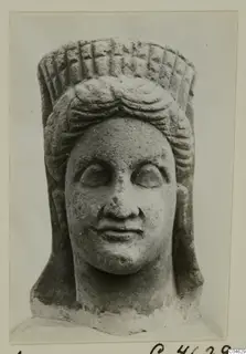 Stone statue head with a tall cylindrical headdress with a grid pattern and layered wavy hair, from Arsos