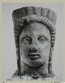 Stone statue head from Arsos, face forward, with a hair band and a tall, fluted headdress.
