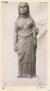 Standing stone statue of a draped female figure from Arsos, photographed against a plain backdrop.
