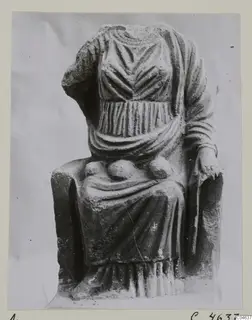 Seated stone statue of a draped figure, head and one forearm missing, photographed on a card mount.