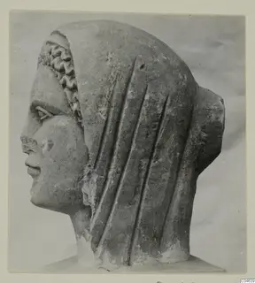 Stone sculpture of a head in profile facing left, with a veil falling in vertical folds and a wavy fringe at the forehead, from Arsos.