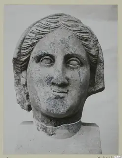 Stone statue head from Arsos, front view, with wavy hair parted at the centre and drawn back over the ears.