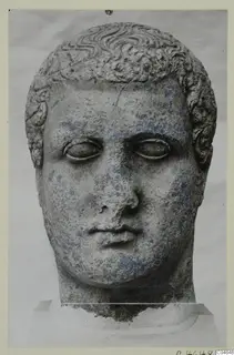 Stone head of a male statue from Arsos, front view, with curled hair and a blank stare.