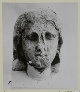 Stone head of a female figure from Arsos, with wavy hair and a broken neck, photographed against a plain background.