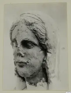Stone statue head from Arsos, a female face with wavy hair over the brow, with the nose and surface worn away.