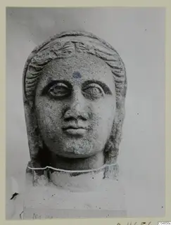 Stone statue head from Arsos, a female face with hair framing it, shown against a plain grey background.