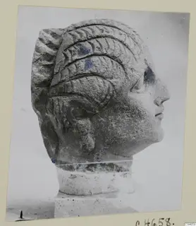 Stone head of a statue from Arsos, shown in profile facing right, with ridged hair and a short neck on a square base