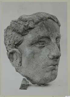 Carved stone head from Mersinaki with short curled hair and a rounded ear, shown against a plain backdrop