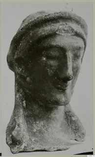 Carved head and upper body of a figure from Mersinaki, shown against a plain grey backdrop