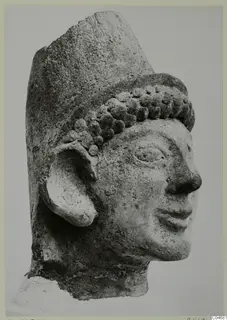 Head of a figure in stone with a tall flat-topped headdress and rows of curled hair, from Mersinaki