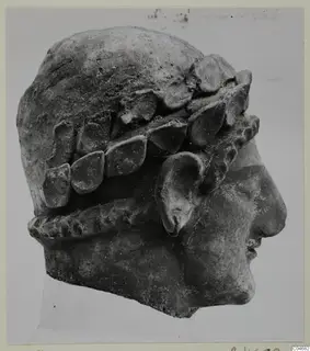 Terracotta head in right profile, with leaf-shaped forms around the head and a twisted band below the ear