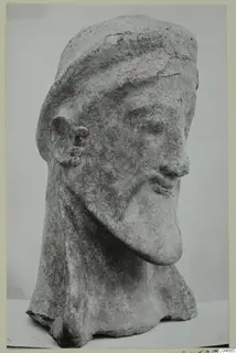 Terracotta head from Mersinaki with a close-fitting cap, long pointed beard and three round ornaments on the ear