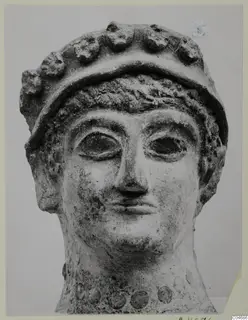 Head of a sculpture with a wide band of rounded knobs across the top and large almond-shaped eyes