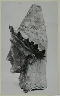 Terracotta head of a figure in profile facing left, wearing a tall cap with a band of pointed ornaments.