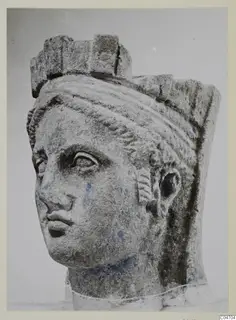 Stone head of a female statue from Arsos, showing a carved face with a polos-like headdress and blue paint traces.