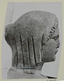 Stone statue head from Arsos, shown in profile to the right with long grooved hair at the back.