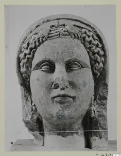Stone head of a female statue from Arsos, face forward, with wavy hair bands framing the forehead.