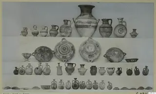 Pottery vessels from Amathus, Tomb 15, arranged in tiers on a light backdrop, with a large jar and many jugs and bowls