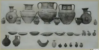 Group of pottery vessels from Amathus Tomb 18: jugs, jars, juglets and bowls arranged in rows on a light cloth.