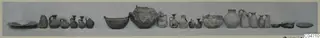 Row of pottery vessels from Amathus, Tomb 4, laid out in a line on a grey ground.