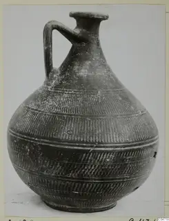 Dark pottery jug with a single loop handle and incised bands, photographed against a pale background, from Amathus