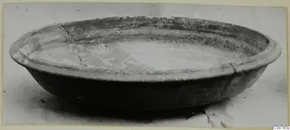 Shallow pottery bowl with a thick rounded rim, seen from the side on a pale surface