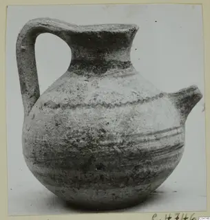 Jug with a strap handle, a trefoil-like spout and a wavy incised band around the shoulder, photographed on a plain surface.