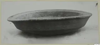 Shallow open bowl with a thick, slightly flaring rim, photographed in side view on a pale surface