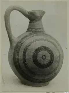 Round-bodied jug with a tall loop handle and concentric circles painted in dark bands on its body.
