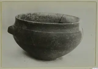 Rounded pottery bowl with a small handle on its left side, photographed on a plain pale background.