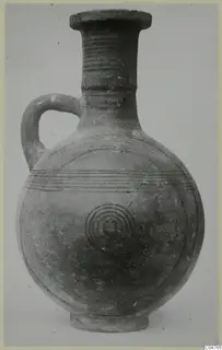 Pottery jug with one loop handle, horizontal grooves on the neck and concentric circles on the body, against a grey background