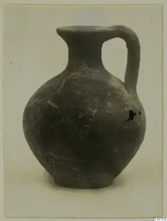 Dark jug with a round body, a single strap handle and a pouring lip.