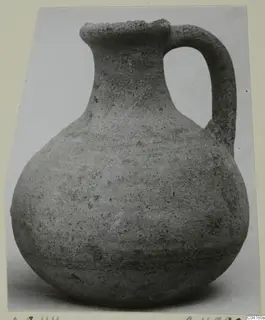 Pottery jug with a round body, narrow neck, flared rim and single strap handle, photographed against a pale background.