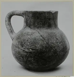 Round-bodied jug with a single loop handle and a short flared neck, cracked, photographed against a plain background.