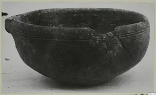 Pottery bowl with a pouring lip on one side, fine incised grooves on the upper body and a crack running down the right side