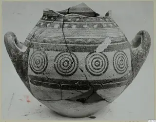 Two-handled jar painted with concentric circles and horizontal bands, shown against a plain background