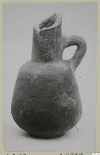 Red slip pottery jug with a trefoil-like spout, single loop handle and rounded body, photographed on a plain background