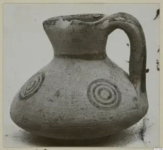 Round-bodied jug with a high neck, strap handle and concentric circle motifs painted on its shoulder