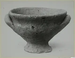 Plain pale pottery footed bowl with two small handles, seen from the side