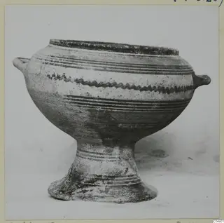 Pedestal bowl with two small handles and painted bands on its body, photographed against a plain background.