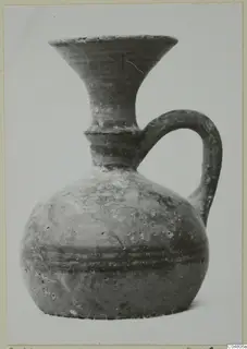 Vessel with a flaring neck, single loop handle and dark horizontal bands on the body, shown alone against a pale backdrop