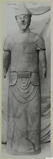 Standing terracotta statue of a bearded figure in a pointed cap, arms at its sides