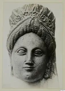 Frontal view of a stone statue head from Arsos, with wavy hair and a tall decorated headdress.