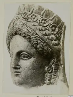 Carved stone head of a woman with rows of wavy hair and rosette ornaments across the top, mounted on a card