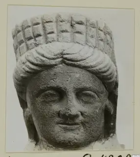 Stone head of a statue from Arsos, front view, with curled hair and a tall headdress marked with a grid pattern