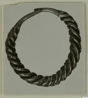 Twisted metal hoop earring from Enkomi, photographed on a grey card