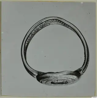 Metal finger ring with an oval bezel and dotted decoration, photographed on a grey background.